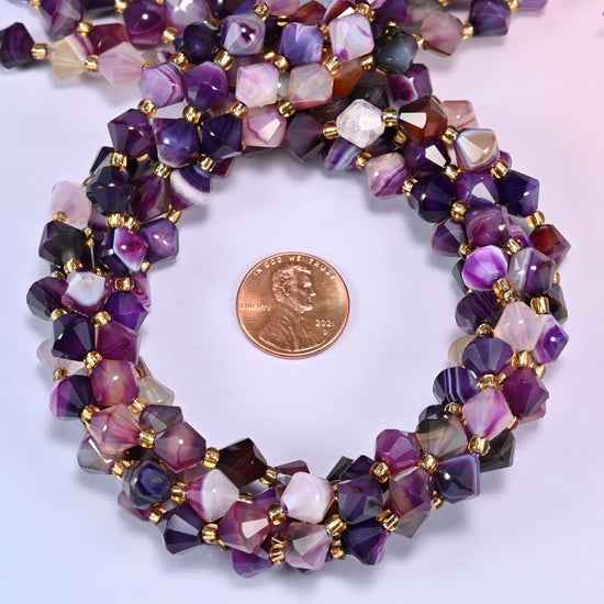 Close-up of 8mm Dyed Purple Strip Agate faceted bicone beads coiled into a circle, showing the deep purple color with lighter banded striping.
