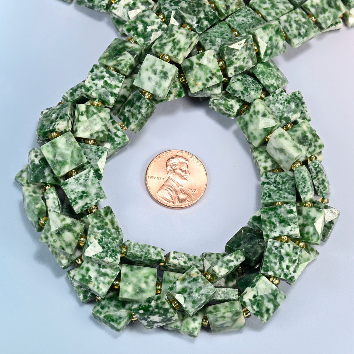 Tree agate faceted flat square beads 10x10mm coiled in a loop around a US penny for scale, close-up of the faceted flat square shape