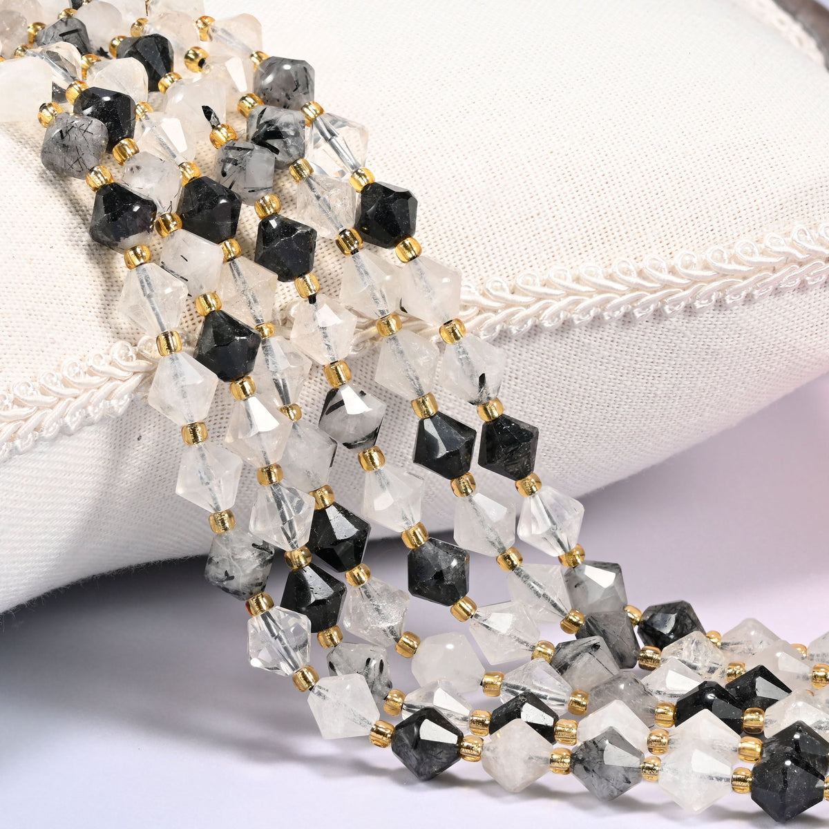 Black rutilated quartz bicone beads laid out on the diagonal in several rows, clear to milky quartz shot through with fine black rutile needles, a gold-tone spacer between every bead.