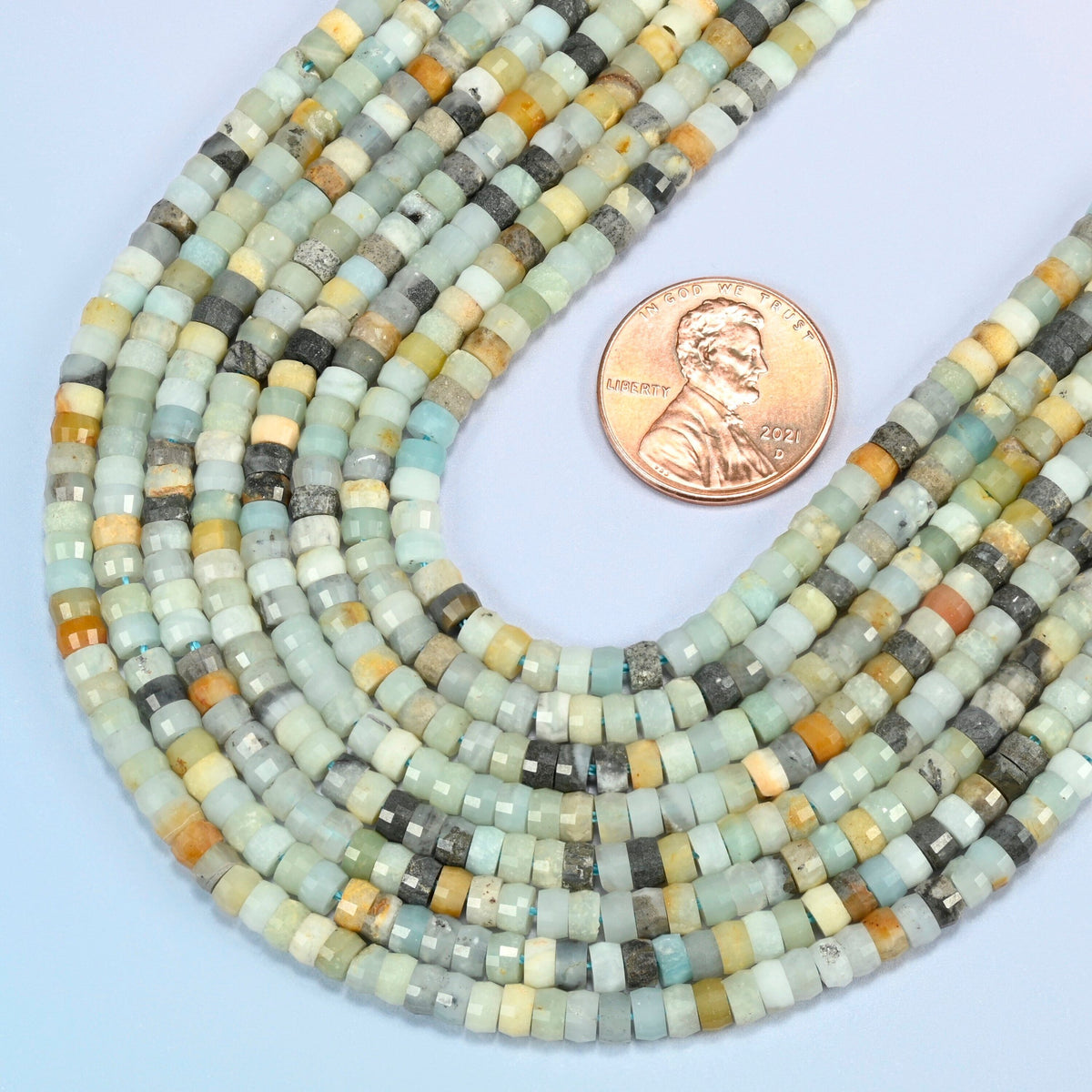 Close view of multi-color amazonite faceted heishi disc strands curving beside a US penny for scale
