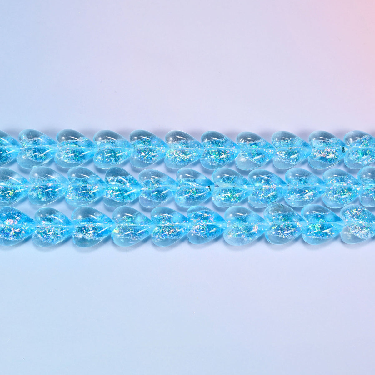 Iridescent light blue heart glass beads seen side on, showing the 8.54mm puffed thickness of each heart