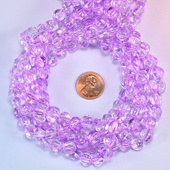 Clear purple pumpkin glass beads coiled tightly, shown with a US penny in the open center for scale.