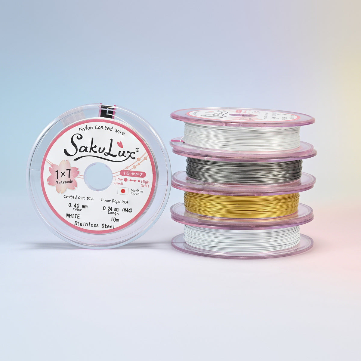 Four rolls of nylon coated stainless steel beading wire stacked beside a spool: white, steel, gold and silver, 7 strand jewelry wire on 10 meter rolls