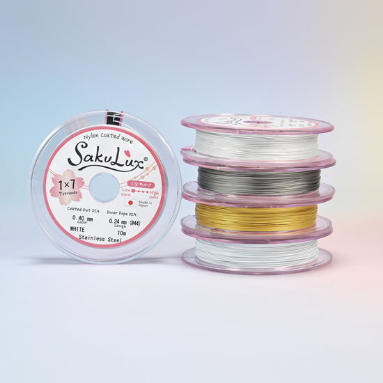 Four rolls of nylon coated stainless steel beading wire stacked beside a spool: white, steel, gold and silver, 7 strand jewelry wire on 10 meter rolls