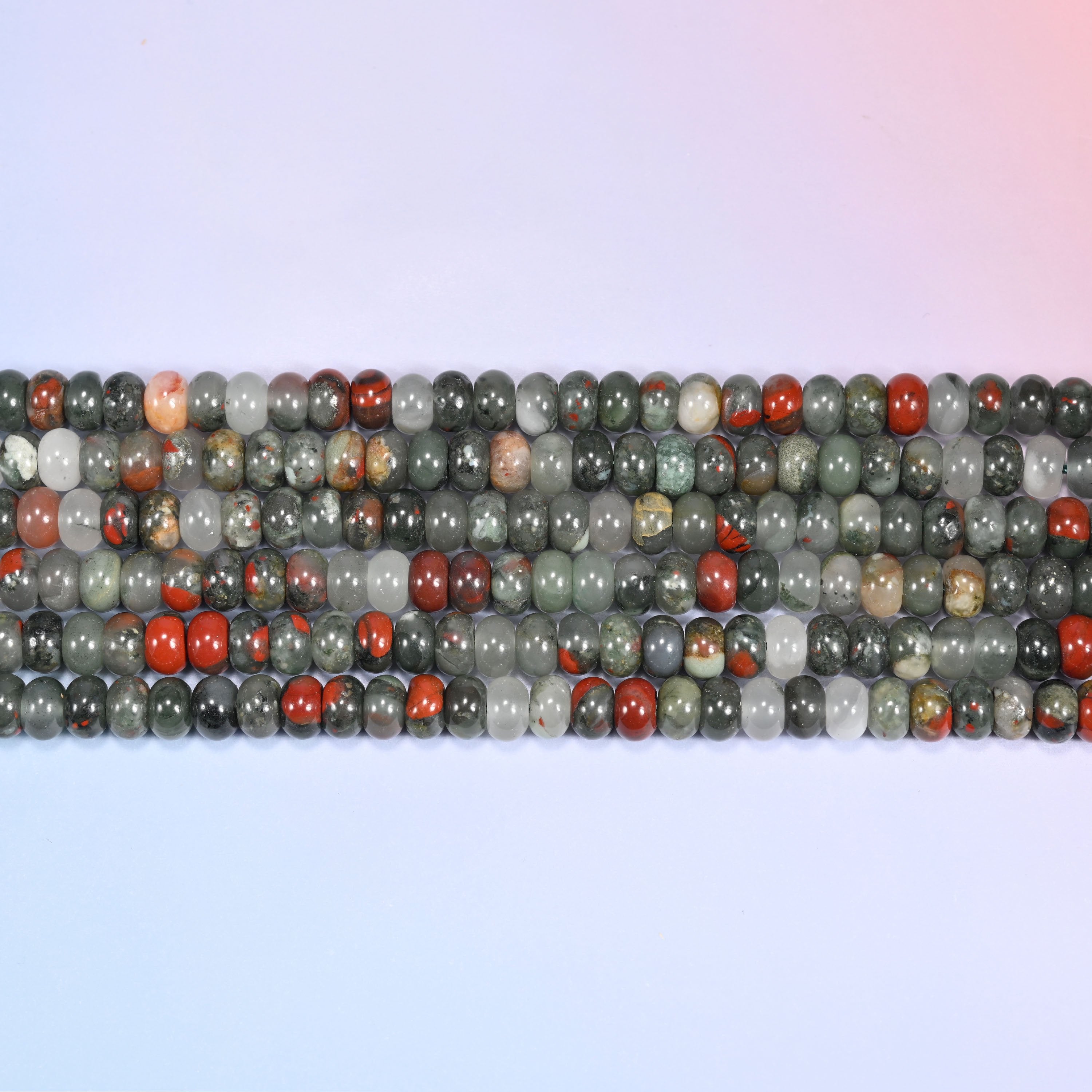 Rows of African Bloodstone round beads laid straight on a lavender surface, showing the natural stone color variation.