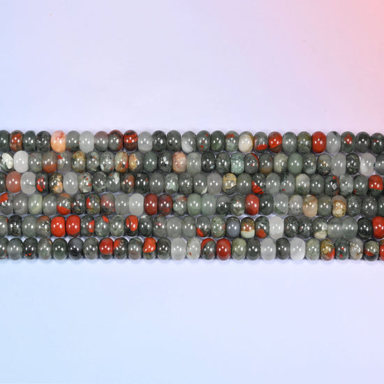 Rows of African Bloodstone round beads laid straight on a lavender surface, showing the natural stone color variation.
