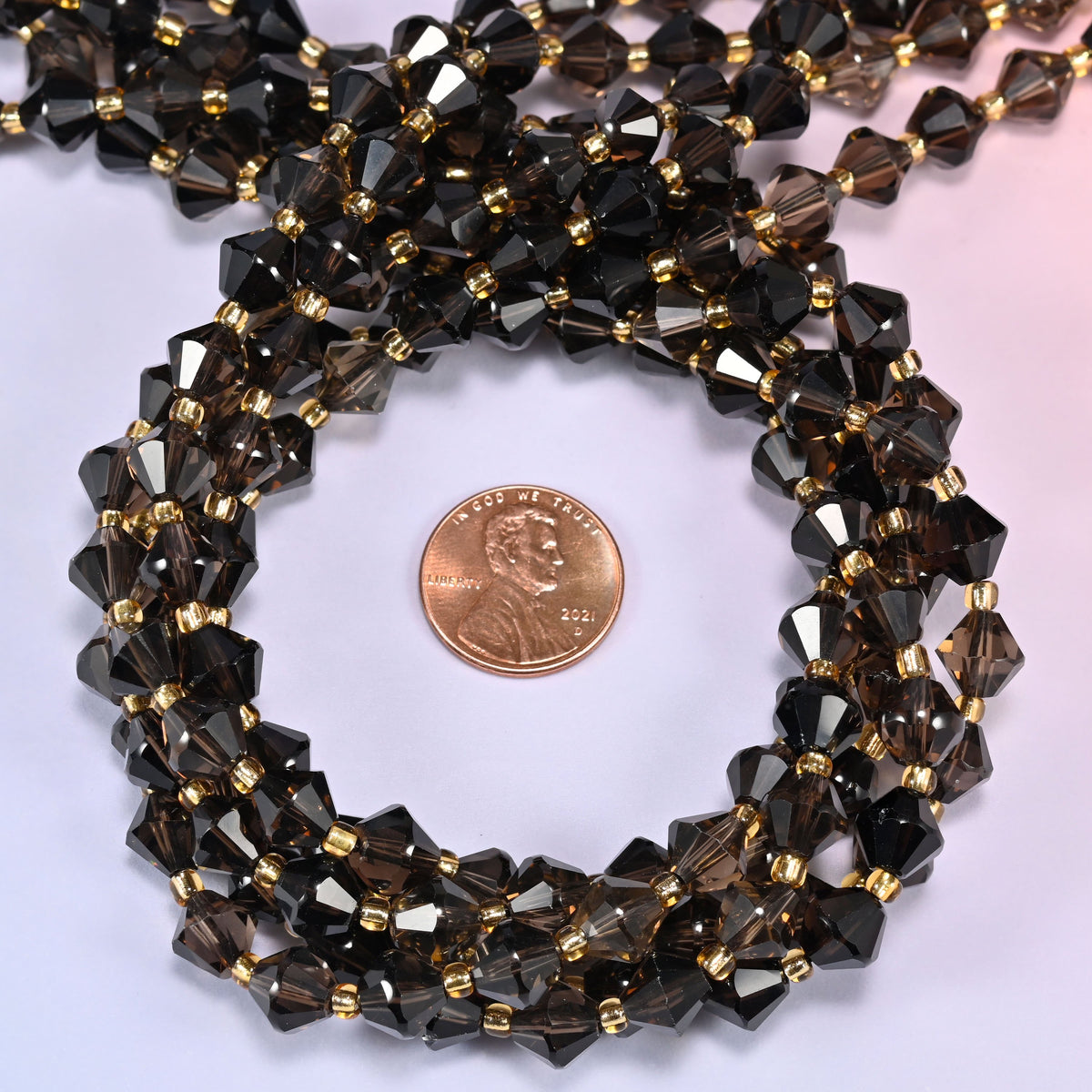 Close-up of 8mm Smoky Quartz faceted bicone beads coiled into a circle, highlighting the translucent brown-gray color and faceted shape.