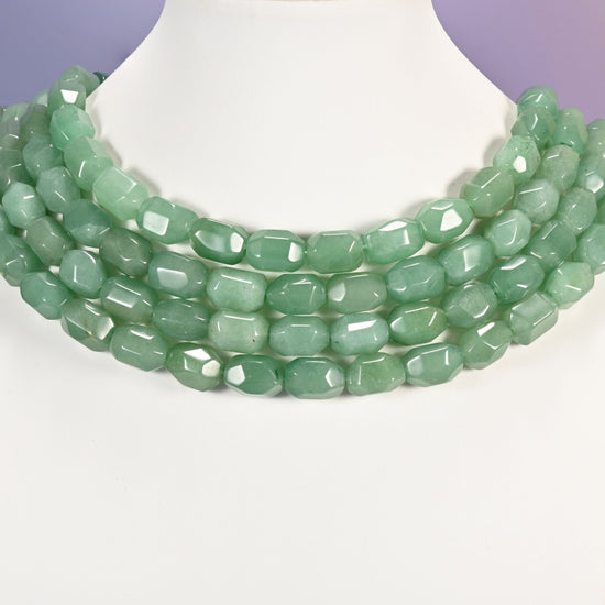 Multi-strand necklace of green faceted Aventurine barrel beads laid on a white mannequin neck form against a lavender background.
