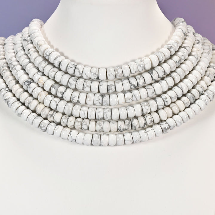 Multi-strand White Howlite necklace laid flat on a mannequin neck form against a lavender background.