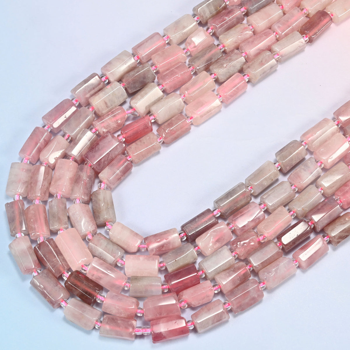 Madagascar multi color rose quartz faceted tube strands sweeping into a wide U fold, soft pink to deep raspberry stone.