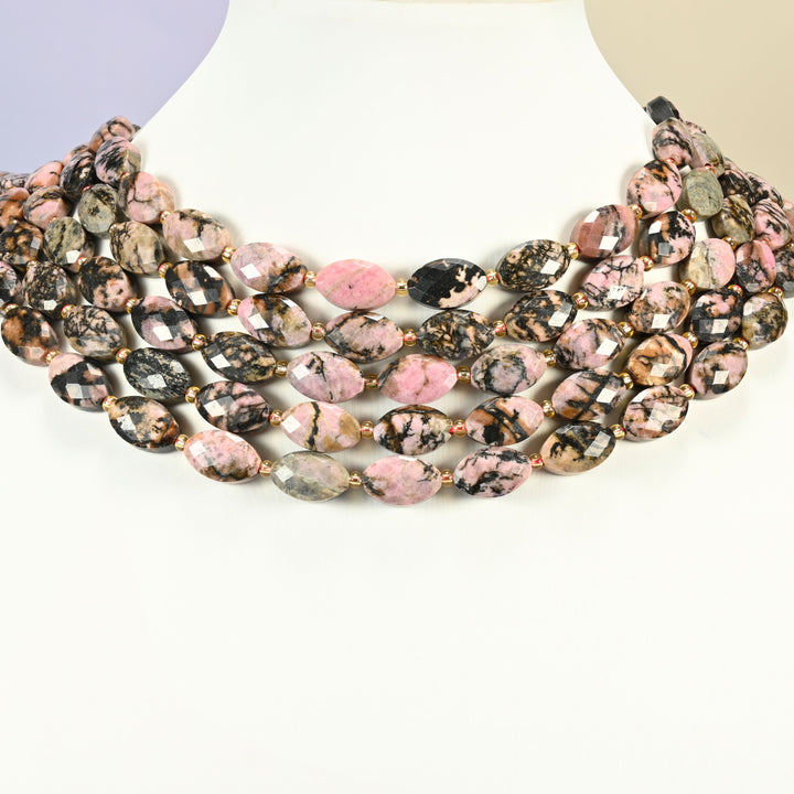 Rhodonite faceted flat oval strands arranged as a layered collar on a white display bust, pink and black beads across the neck
