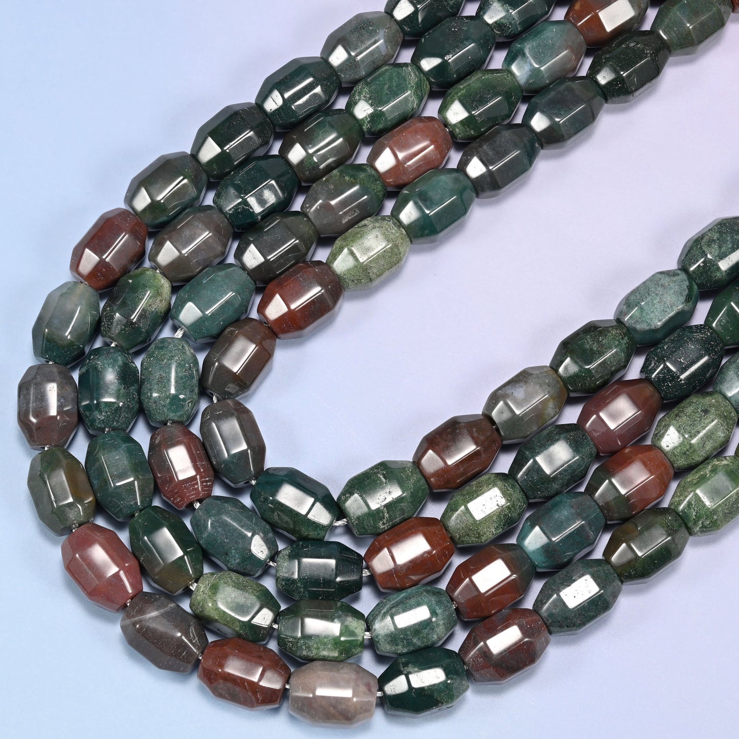 Close-up of a circular coil of Indian Agate faceted barrel beads on a light lavender background.