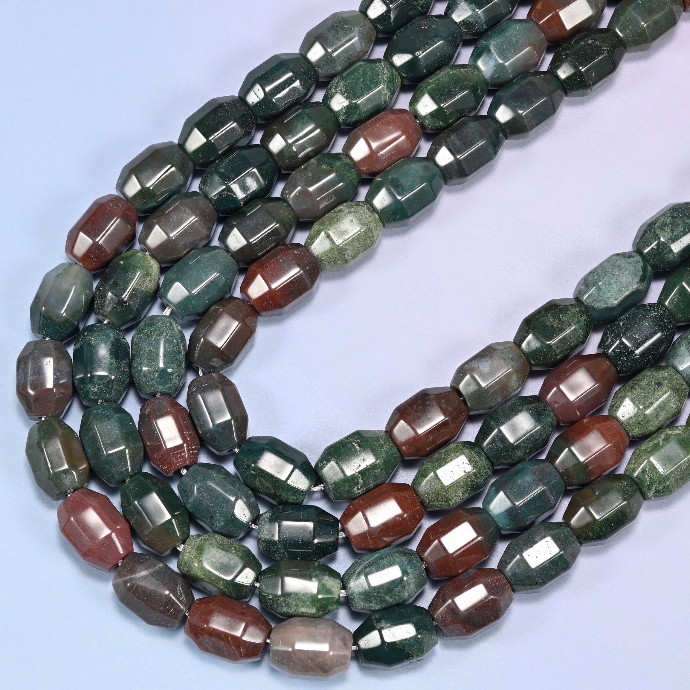 Close-up of a circular coil of Indian Agate faceted barrel beads on a light lavender background.
