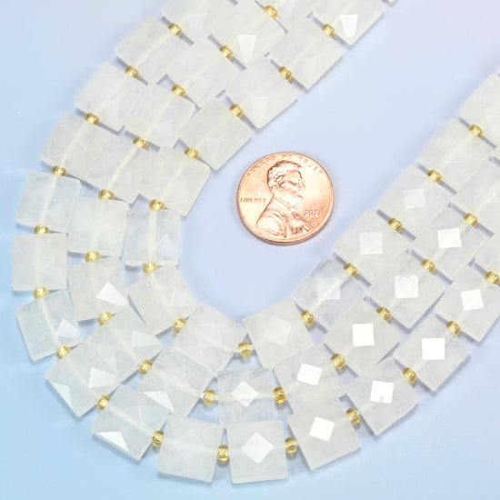 Close view of clear quartz faceted flat square strands curving beside a US penny for scale