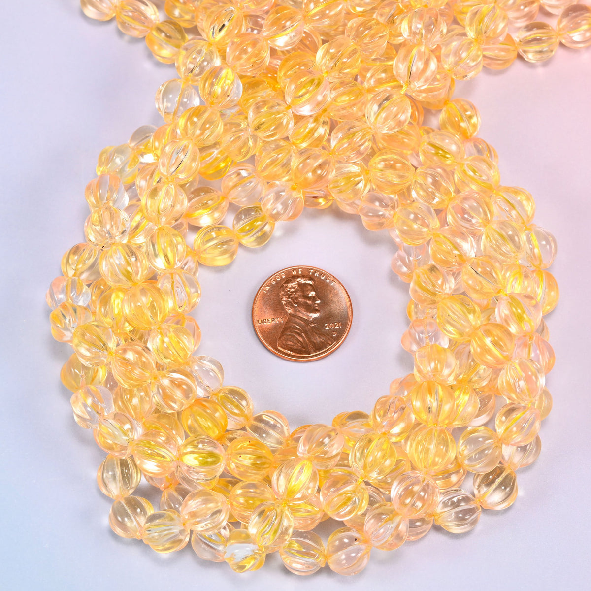Yellow clear pumpkin glass beads coiled tightly, shown with a US penny in the open center for scale.