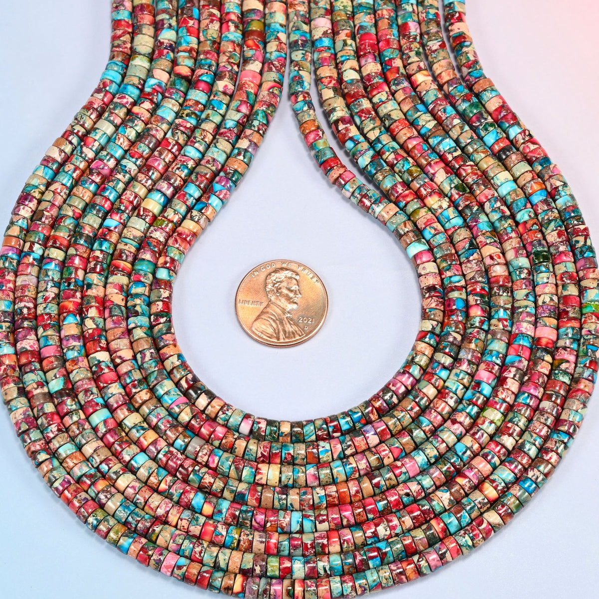 Dyed pink blue sea sediment jasper heishi disc strands formed into a teardrop loop around a US penny for scale