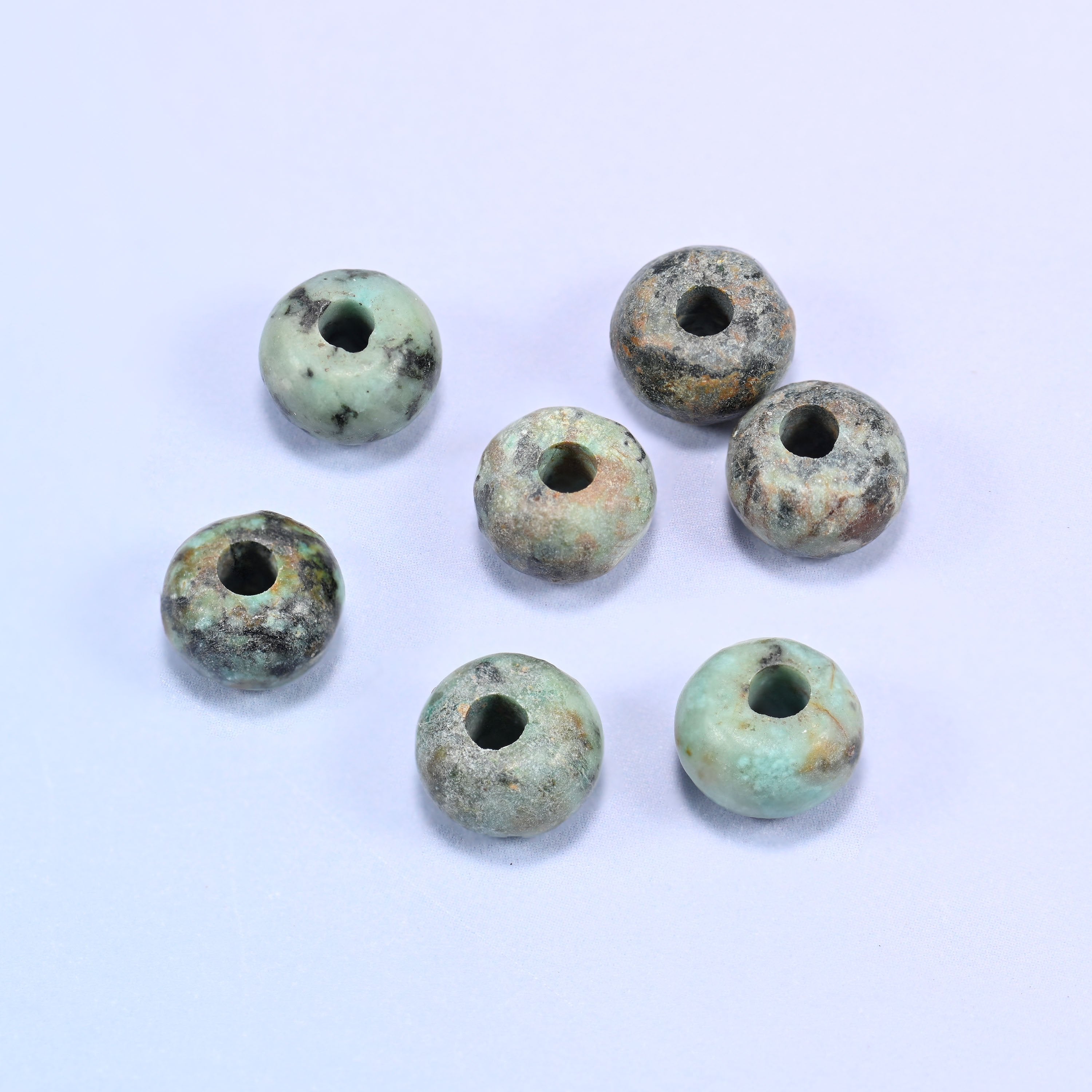 Close-up of individual loose African Howlite beads laid out on a white surface, showing the large center-drilled hole and varied coloring of each bead.