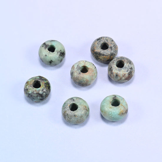 Close-up of individual loose African Howlite beads laid out on a white surface, showing the large center-drilled hole and varied coloring of each bead.