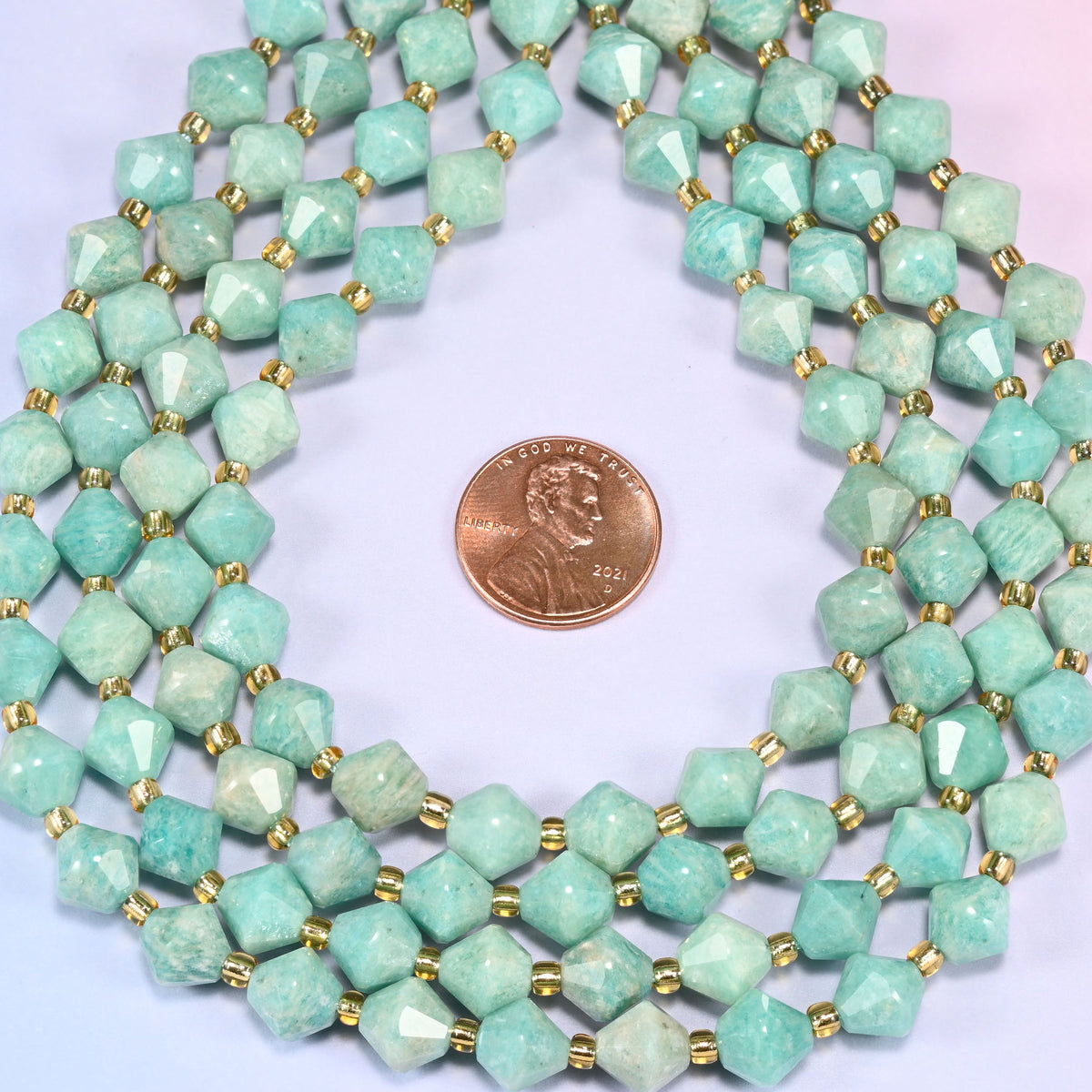 Green Amazonite faceted bicone beads 8mm with gold-tone spacers, strand coiled into a neat circle with a penny centered for scale