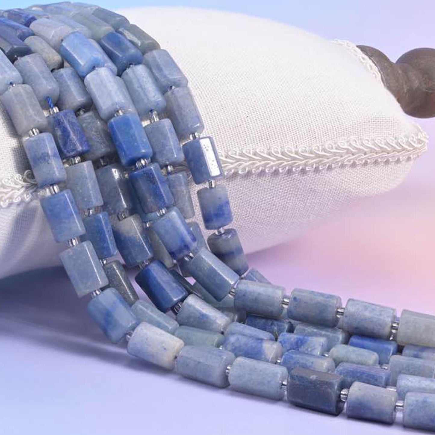 Blue aventurine faceted tube strands resting over a white cushion, soft denim blue rectangular beads