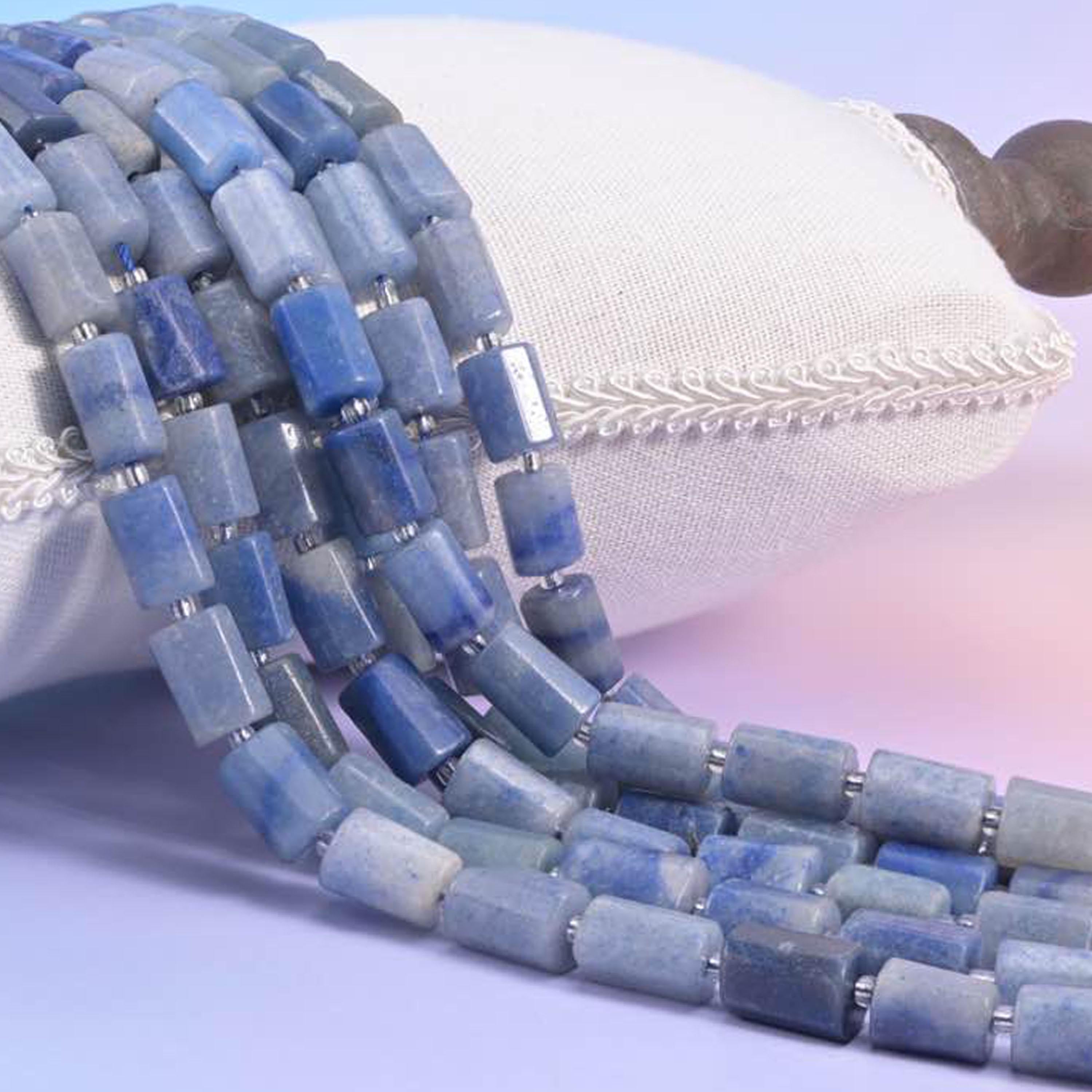 Blue aventurine faceted tube strands resting over a white cushion, soft denim blue rectangular beads