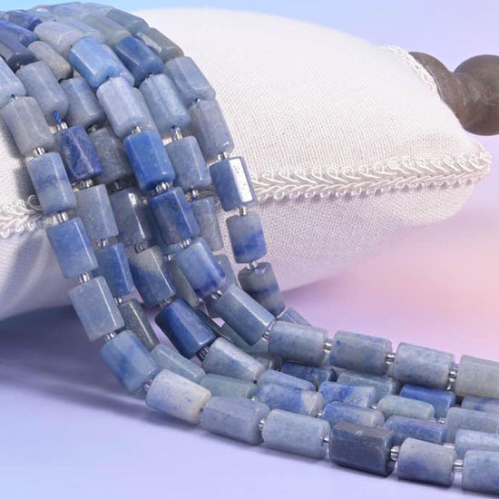 Blue aventurine faceted tube strands resting over a white cushion, soft denim blue rectangular beads