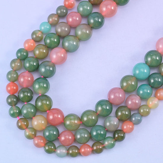 Green Yanyuan Agate smooth round beads, strands curving across a lilac background, olive green beads beside peach and pink ones