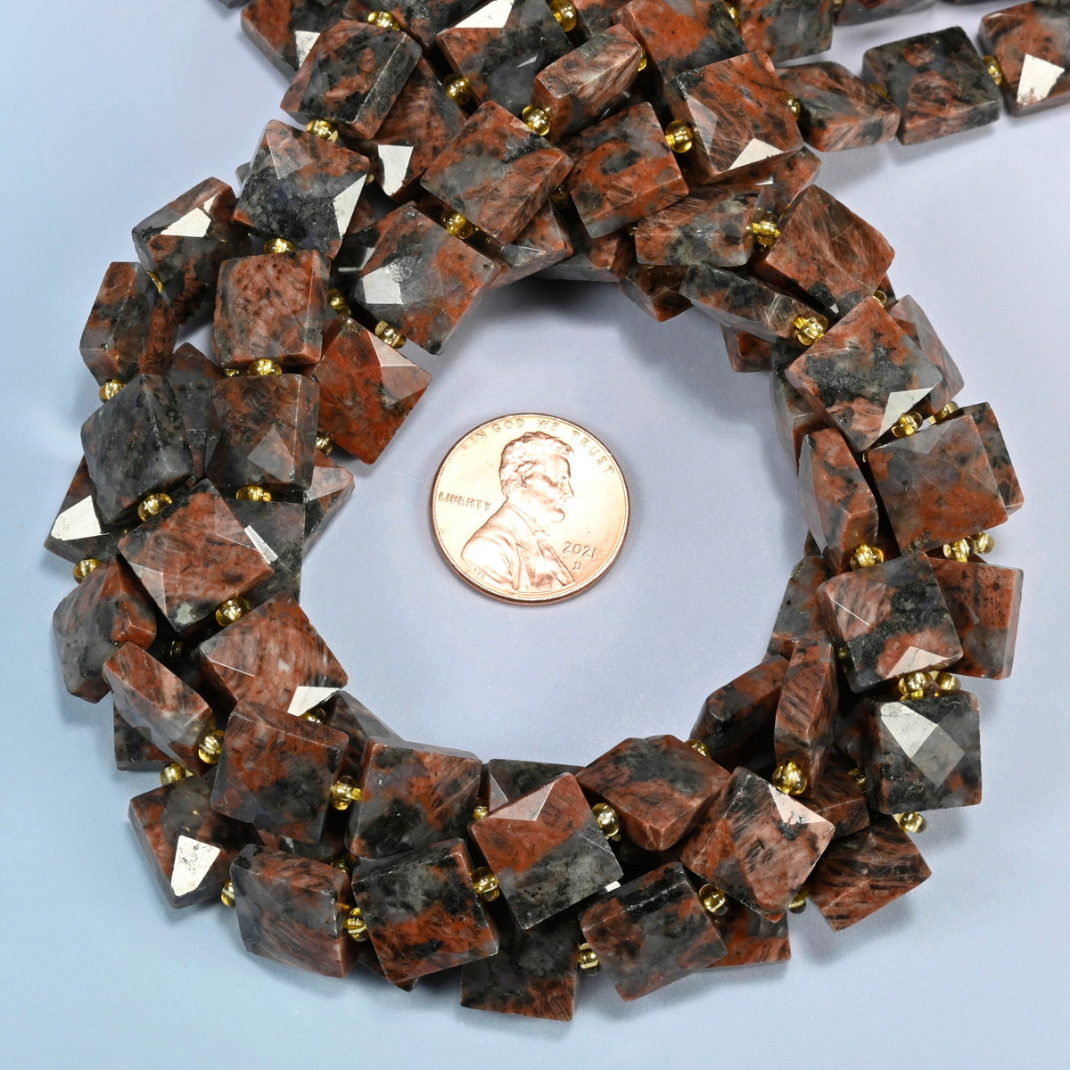 Natural red sesame jasper faceted flat square beads 10x10mm coiled in a loop around a US penny for scale, close-up of the faceted flat square shape