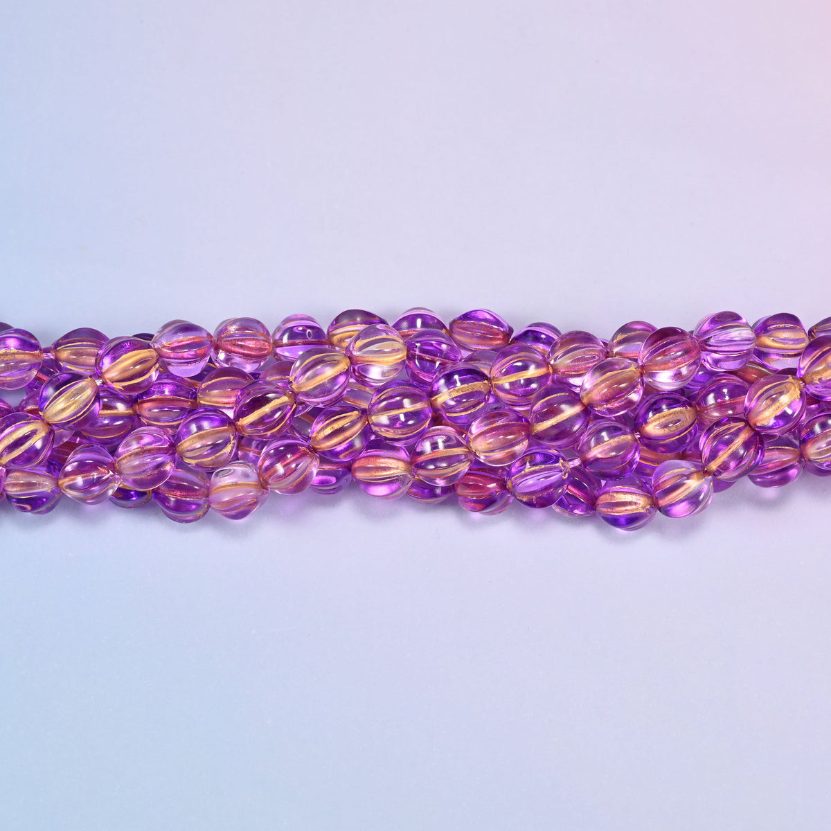Purple gold pumpkin glass beads, 8mm melon rounds, strands laid in a gentle wave straight across the frame.