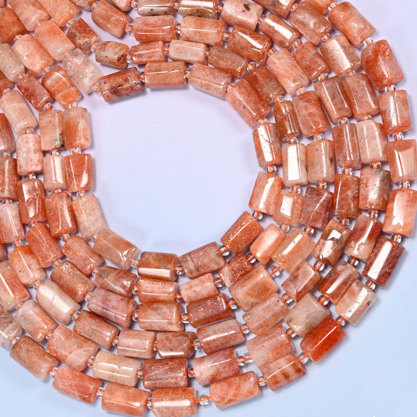 Bundled coil of faceted Golden Strawberry Quartz tube beads on a lavender background with a penny placed at the center for scale.