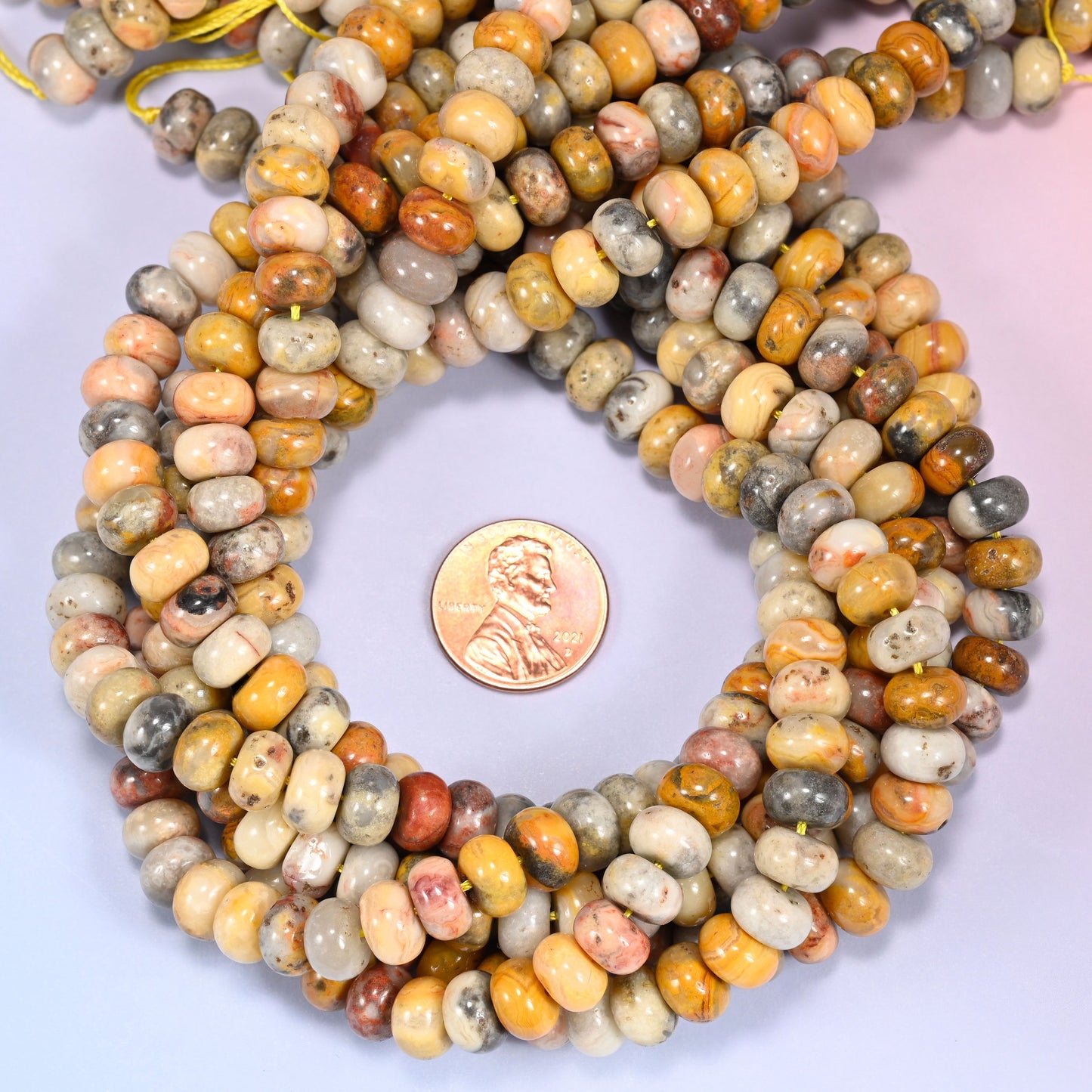 Multiple strands of Crazy Agate beads gathered together on a lavender surface, loose ends visible.