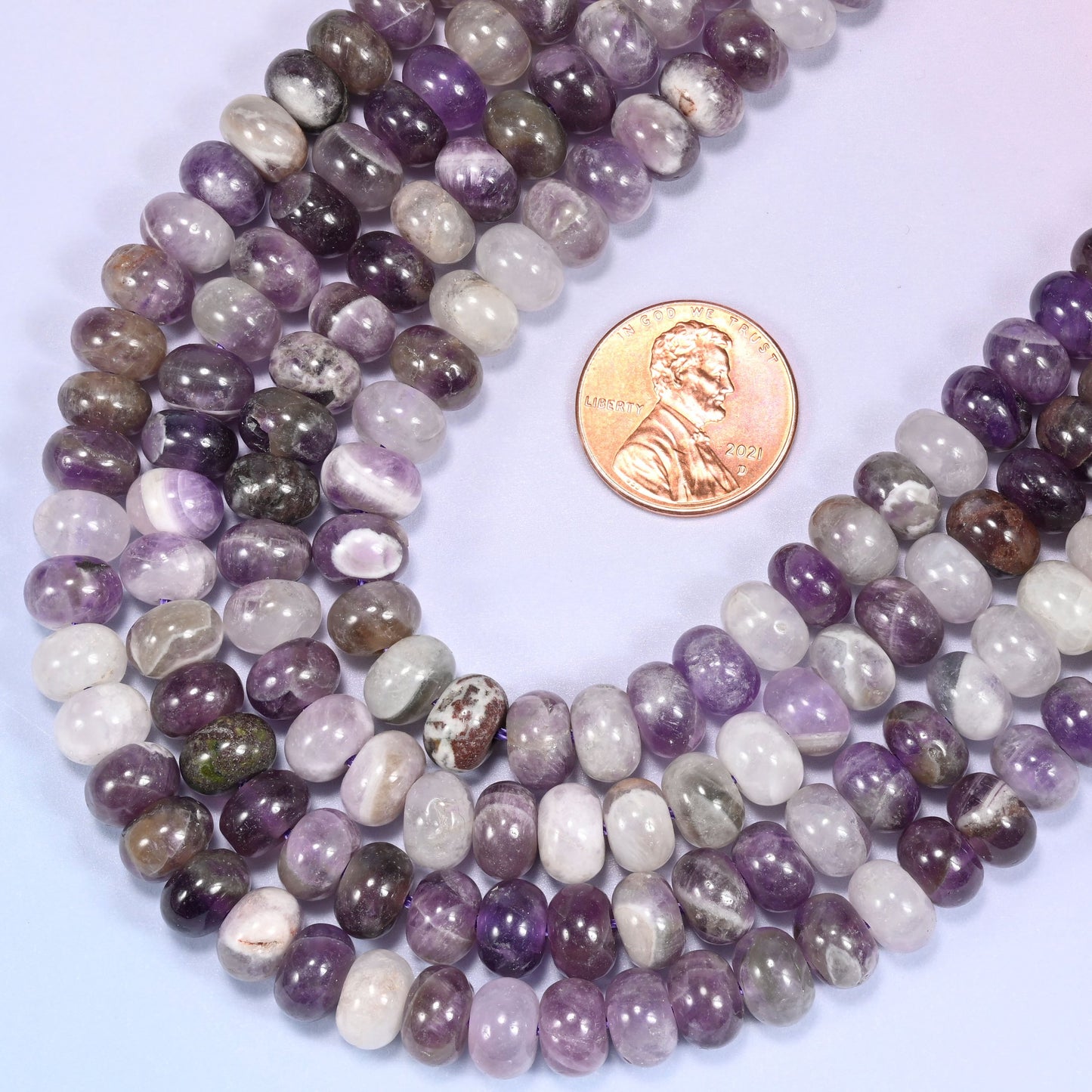Rows of Amethyst rondelle beads laid straight on a lavender surface, showing the natural stone color variation.