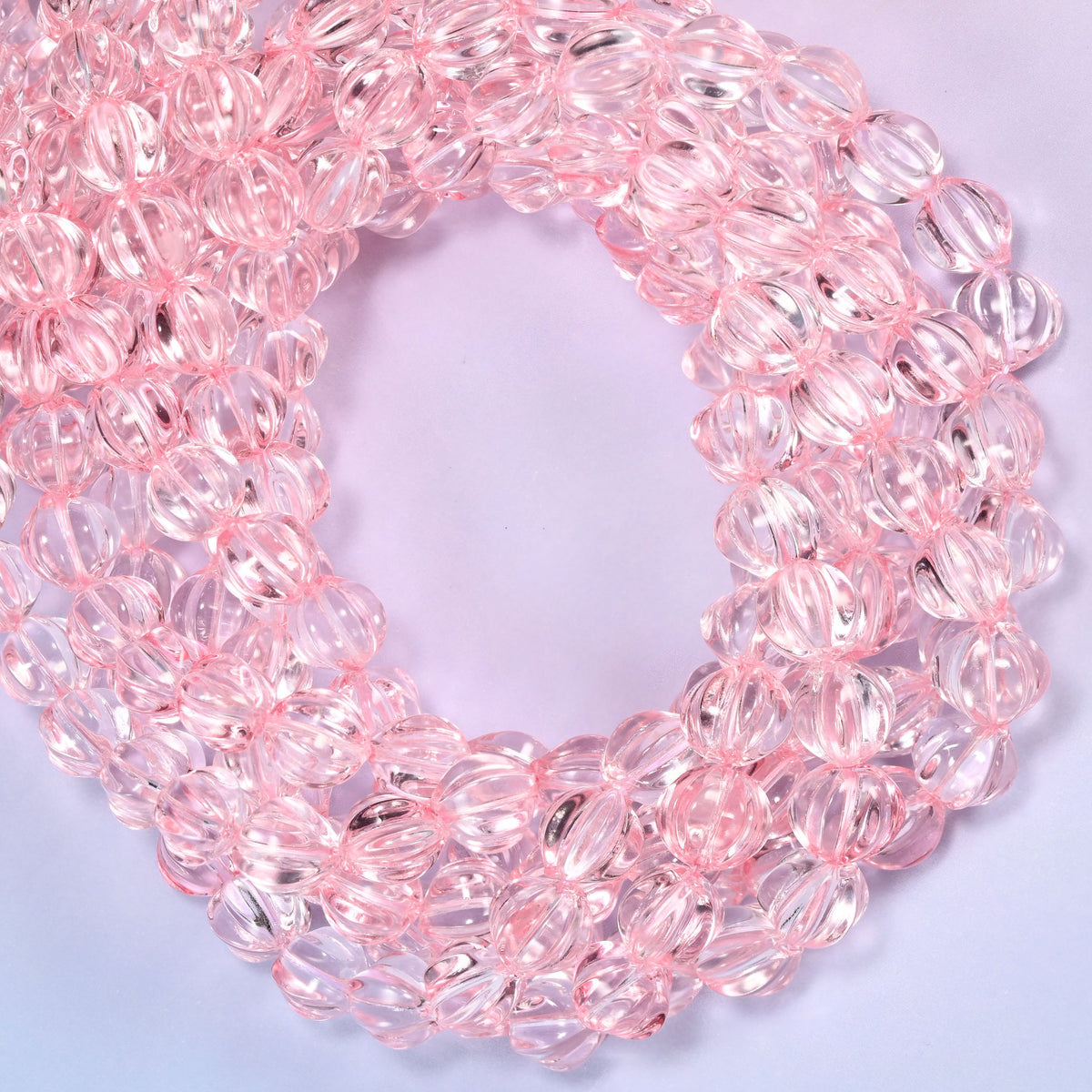 Clear pink pumpkin glass beads coiled with the open center to one side, showing the fluted grooves end on.