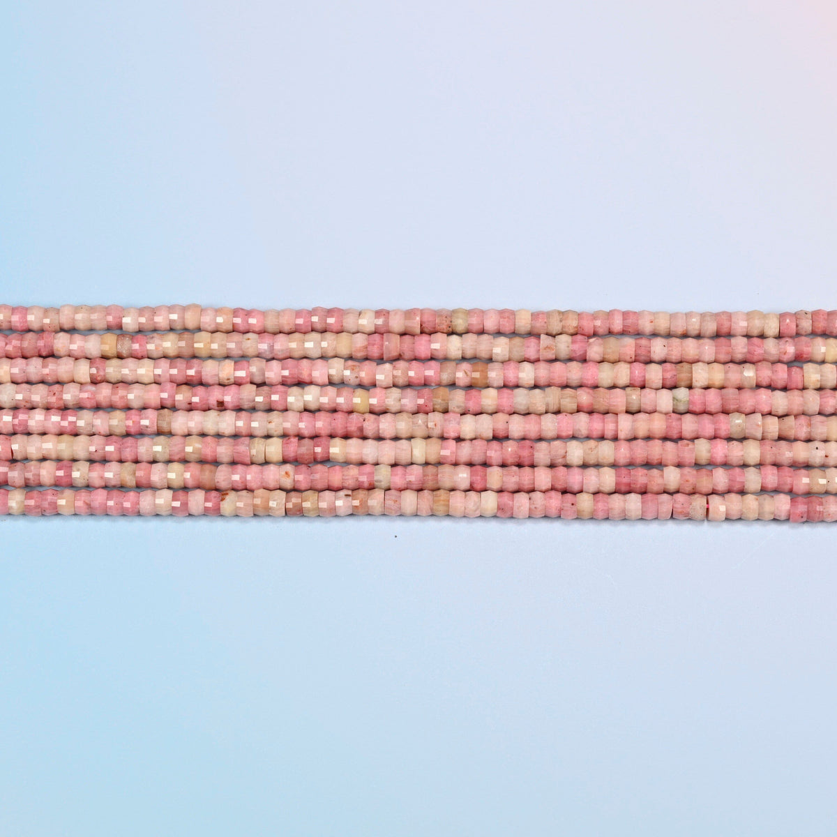 Several strands of pink rhodonite faceted heishi disc beads laid in straight rows