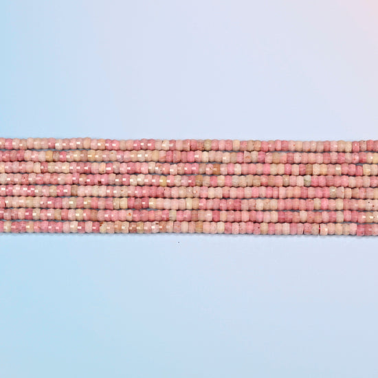 Several strands of pink rhodonite faceted heishi disc beads laid in straight rows