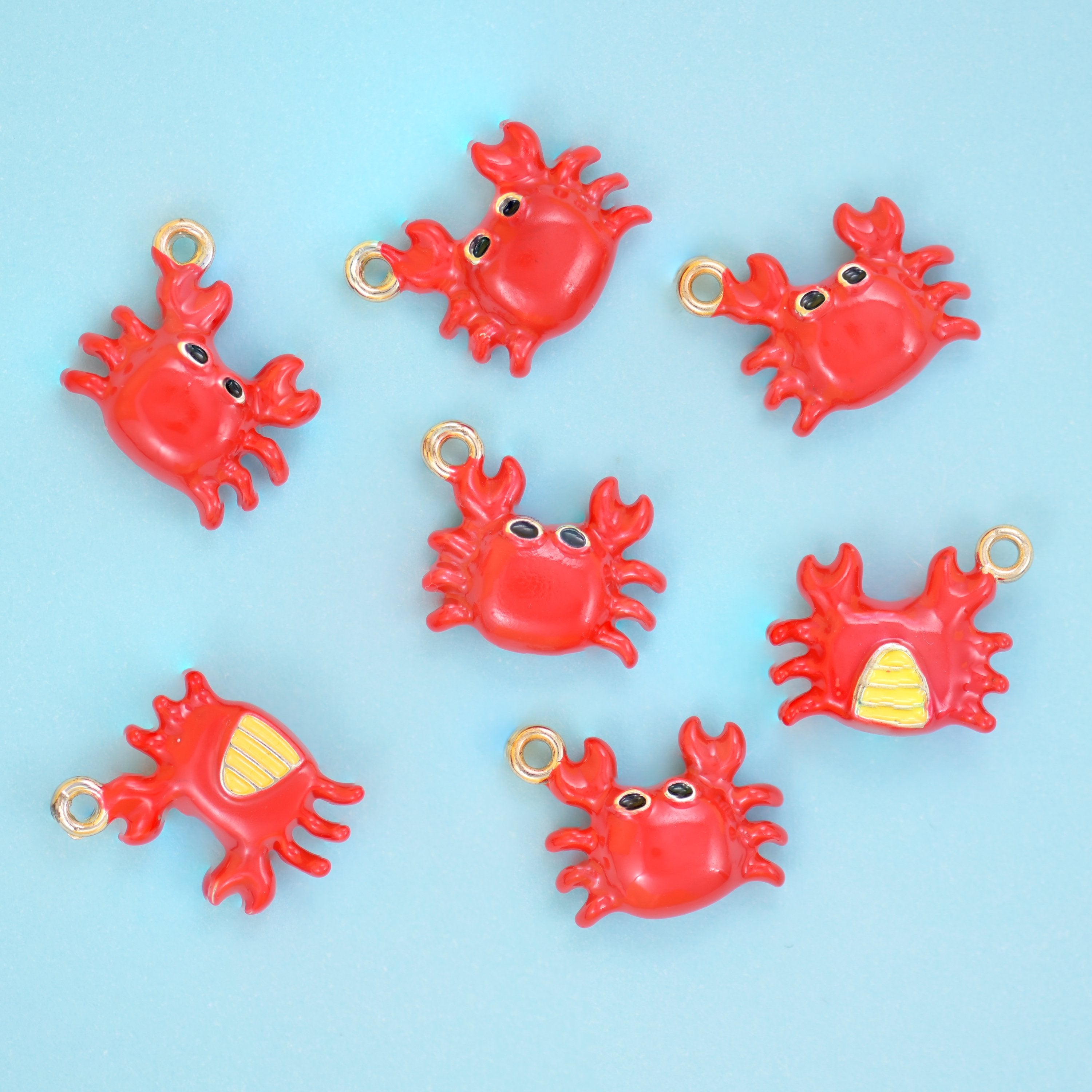 Enamel crab charms scattered together, red enamel bodies with raised claws and legs over 18K gold plated brass