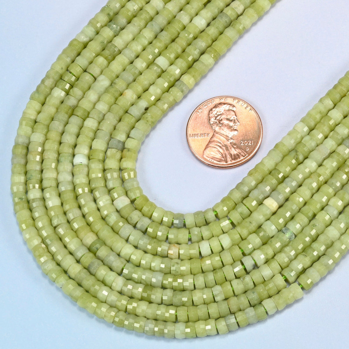 Close view of South Jade faceted heishi disc strands curving beside a US penny for scale