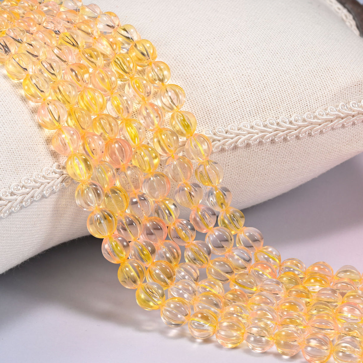 Yellow clear pumpkin glass beads, 8mm fluted melon rounds, several strands draped over a white cushion.
