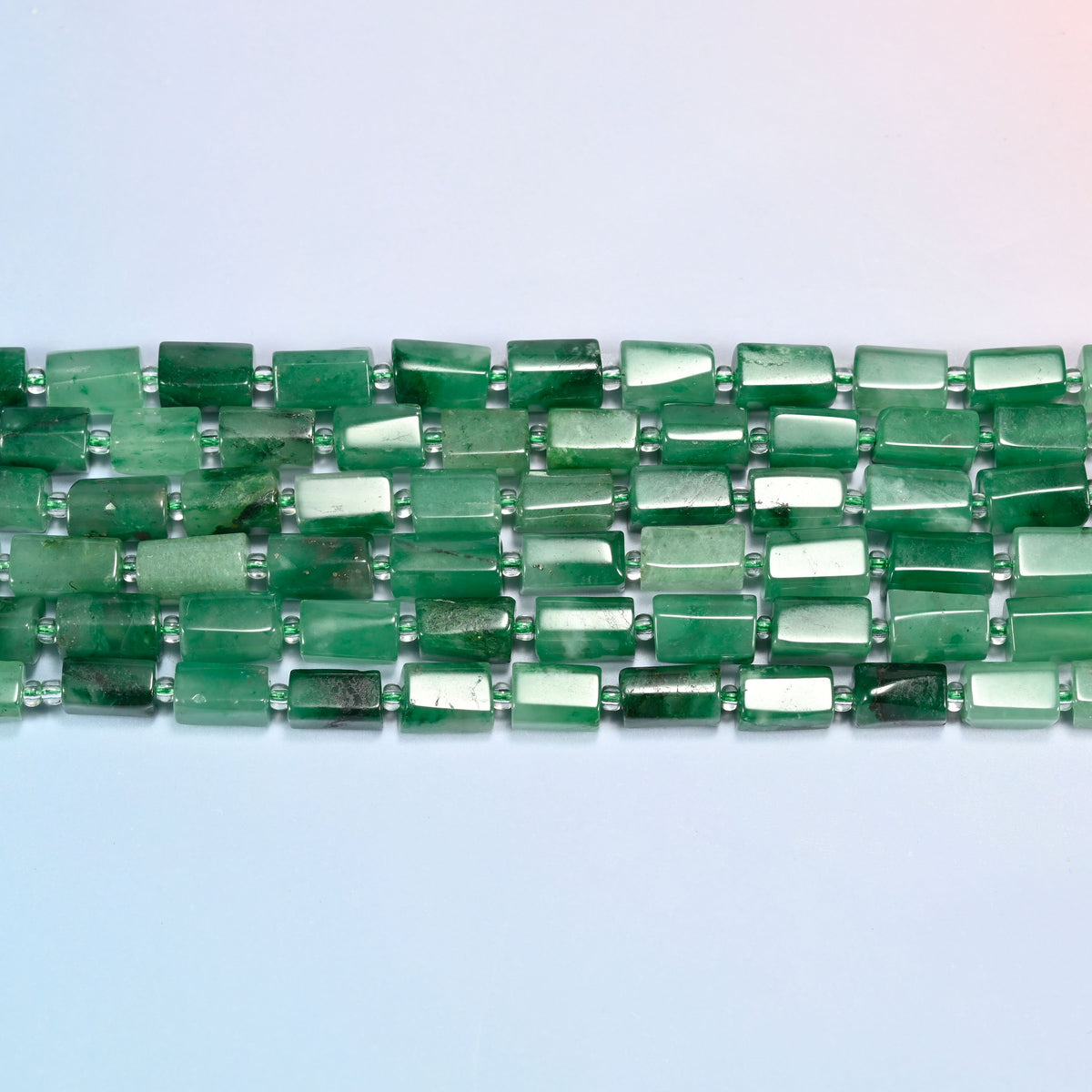 Several strands of African jade faceted tube beads laid in straight rows with light green seed bead spacers