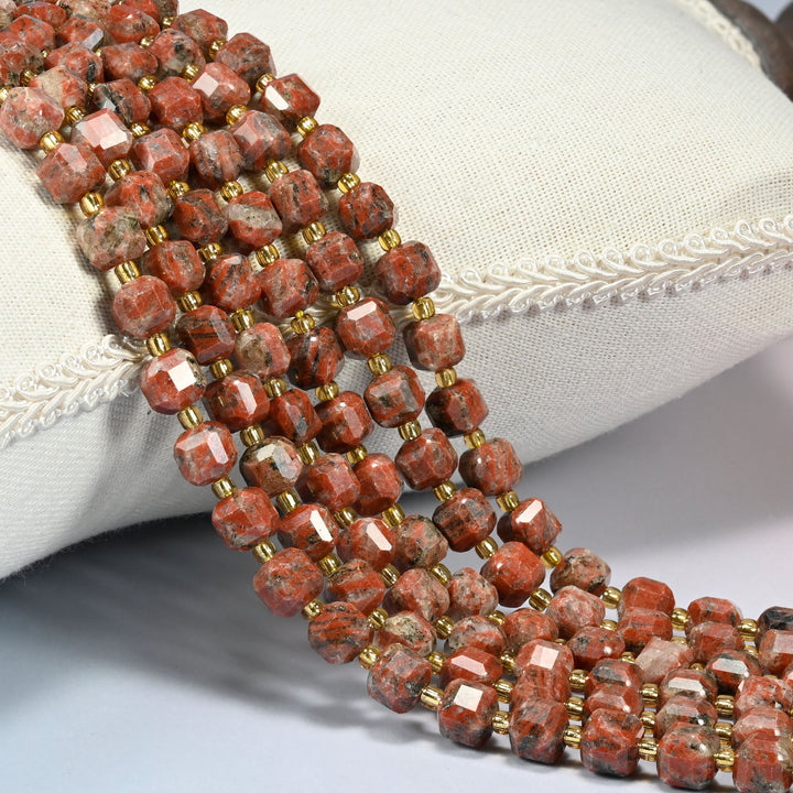 Red sesame jasper faceted cube beads 6mm with small gold spacer beads, several strands draped over a white cushion