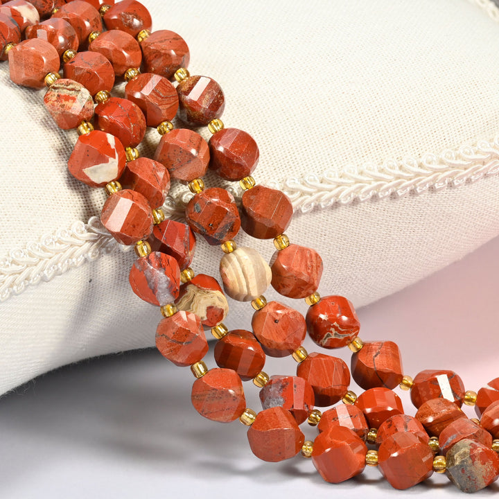 Flower red jasper faceted spiral twist beads 10mm with small gold spacer beads, several strands draped over a white cushion