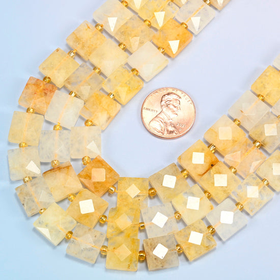 Close view of natural golden healer quartz faceted flat square strands curving beside a US penny for scale
