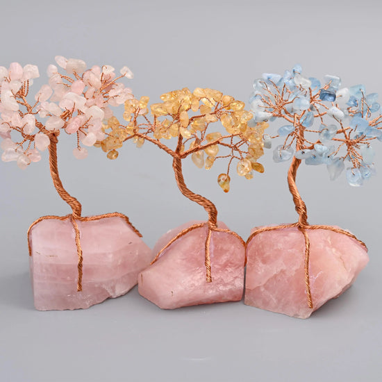 A chunk of raw pink rose quartz with a copper wire trunk and branches loaded with polished gemstone chips