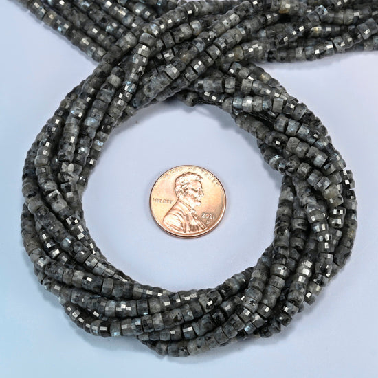 Black labradorite faceted heishi disc beads 2x4mm coiled in a loop around a US penny for scale, close-up of the faceted disc shape