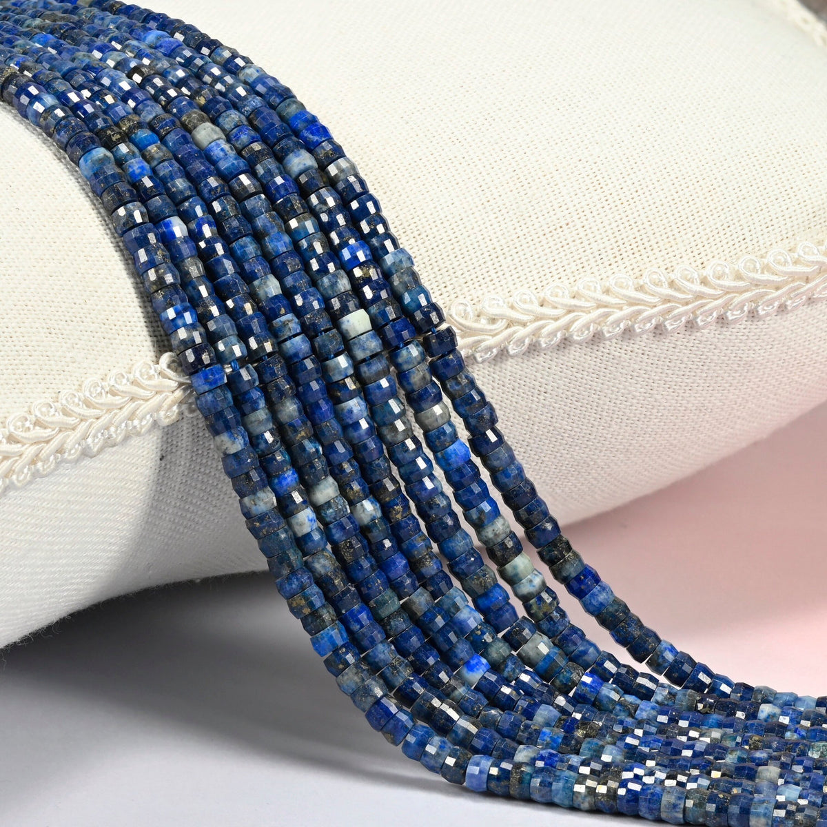 Dark blue lapis faceted heishi disc beads 2x4mm, several strands draped over a white cushion