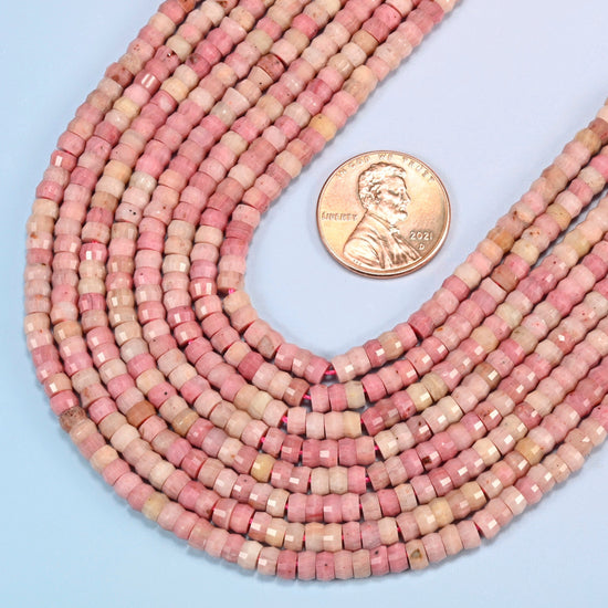 Close view of pink rhodonite faceted heishi disc strands curving beside a US penny for scale