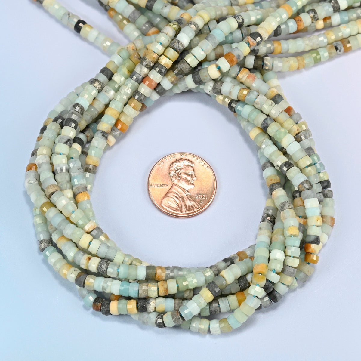 Multi-color amazonite faceted heishi disc beads 2x4mm coiled in a loop around a US penny for scale, close-up of the faceted disc shape