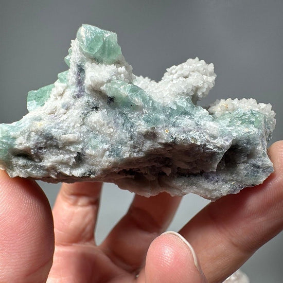 Hand holding a plate of mint green fluorite cubes set among knobbly white quartz