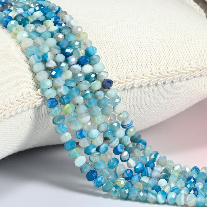 Dyed Blue Strip Agate gemstone rondelle beads 4x6mm faceted, strand draped over a cream fabric cushion