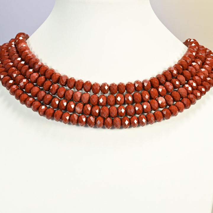 Dark red jasper faceted rondelle strands arranged as a layered collar on a white display bust, brick red beads across the neck